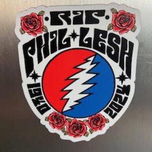 May include: A black and white sticker with a red, white, and blue circle in the center. The circle has a lightning bolt design and the text "R.I.P. Phil Lesh 1940-2023" around the outside. The sticker is surrounded by four red roses.