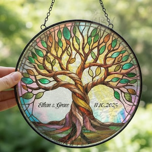 May include: A round stained glass window featuring a tree design with a brown trunk and colorful leaves. The window has a black metal frame and a chain for hanging. The names "Ethan & Grace" and the date "11.10.2025" are displayed.
