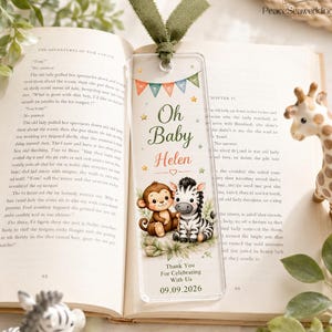May include: A clear acrylic bookmark with a green ribbon, featuring a colorful bunting, stars, and illustrations of a cartoon monkey and zebra. The text reads Oh Baby Helen, Thank You For Celebrating With Us, and the date 09.09.2026.