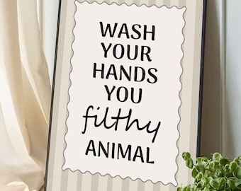 May include: A rectangular framed wall art print featuring a beige and white vertical striped background. Centered is a scalloped-edge white plaque with the black text: WASH YOUR HANDS YOU filthy ANIMAL. The frame is thin and black in color.