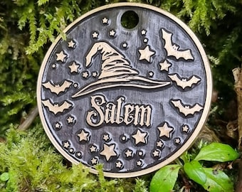 May include: A round, black metal charm with a gold witch's hat, bats, and stars. The charm says "Salem" in gold lettering.