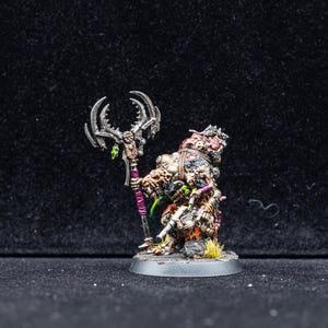 Può includere: Figurina in miniatura di una creatura mutata grottesca con un bastone. La figura è dipinta con tonalità marroni, verdi e viola. Il bastone ha una testa argentata e un'impugnatura viola. La figura è su una base grigia.