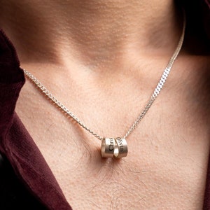May include: A silver chain necklace with a pendant made of three stacked rings. Each ring has a different word engraved on it.