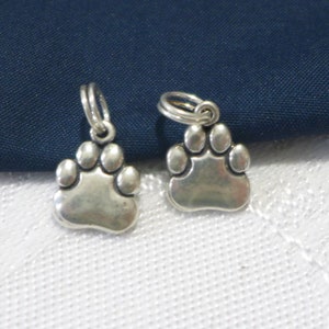 May include: Two silver paw print charms with a loop for attaching to a necklace or bracelet.