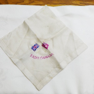 May include: A white linen handkerchief with embroidered flags of the United Kingdom and Canada, and the text "FROM CANADA".