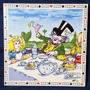 May include: Square ceramic tile featuring a colorful illustration of the Mad Hatter's tea party from Alice in Wonderland. The image includes Alice, the Mad Hatter, the March Hare, and a table set with tea, cakes, and a teapot. The border has a playing card design.