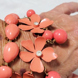 May include: A coral pink bracelet with flower charms and round beads. The bracelet is made of metal and has a gold finish.