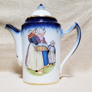May include: A blue and white ceramic teapot with a handle and spout. The teapot is decorated with a scene of three people in traditional Dutch clothing, holding a basket of flowers. The teapot has a gold trim around the top and bottom.