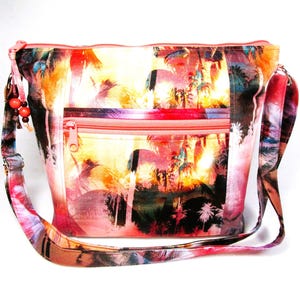 May include: A colorful shoulder bag with a tropical sunset design. The bag features a zippered front pocket and a long, adjustable strap. The main colors are orange, pink, and yellow, with palm tree silhouettes. The bag has a coral-colored zipper and trim.