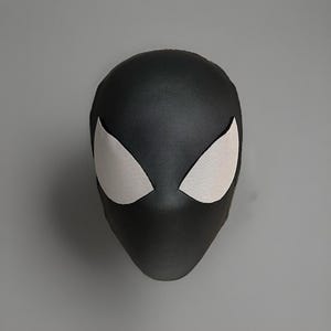 May include: A black superhero mask with white mesh eye coverings. The mask is a solid black color and has a smooth texture. The eye coverings are in a triangular shape.
