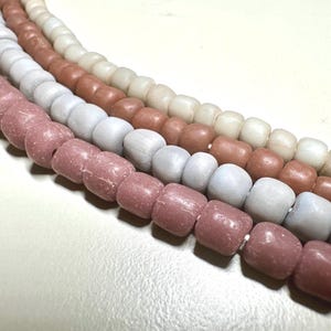 Puede incluir: Cuatro hilos de cuentas en varios colores: rosa empolvado, gris claro, marrón y blanco roto. Las cuentas son cilíndricas con bordes redondeados, ensartadas para formar collares o elementos decorativos. Acabado mate.