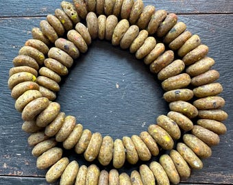 May include: Strand of olive-colored, oval-shaped beads with speckled accents of yellow, orange, and black. The beads are strung on a cream-colored cord. The beads have a textured, organic appearance.