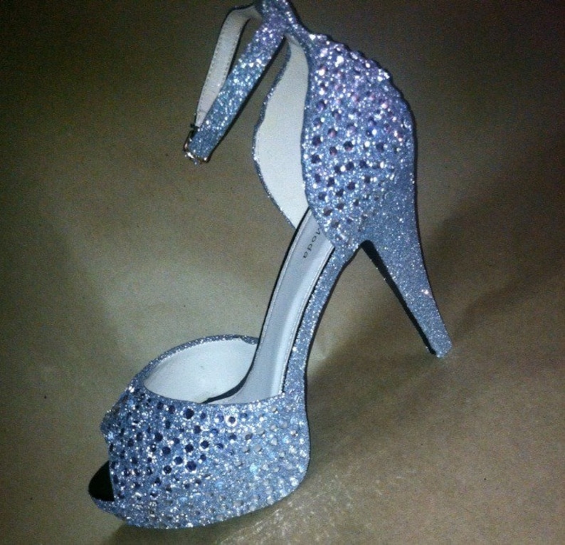 May include: A silver high-heeled sandal covered in sparkling rhinestones. The sandal has a peep-toe design and an ankle strap.