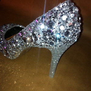 May include: Silver high-heeled shoe covered in sparkly sequins. The shoe has a pointed toe and a thin heel.