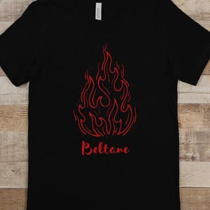 May include: Black t-shirt featuring a red stylised flame design with the word "Beltane" printed below it.