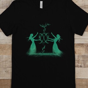 May include: Black t-shirt featuring a green design of two figures holding hands around a circle with a plant growing from the centre.