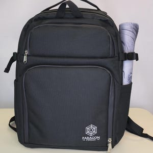 May include: Black backpack with multiple compartments, a top handle, and side pockets. A rolled-up patterned item is secured in a side pocket. The backpack has a logo that says "Paragon Forge".