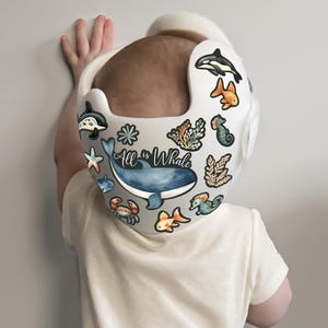 Op de afbeelding: Een witte helm met een blauwe walvis, een zeepaardje, een sterretje en andere stickers met een oceaan thema. De tekst "All is Whale" staat op de helm.