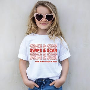 以下が含まれることがあります： 赤色の「SWIPE & SCAN」という文字が繰り返された白いTシャツ。下に「Look At Me Swipe & Scan」と書かれています。ハート型のサングラスをかけています。