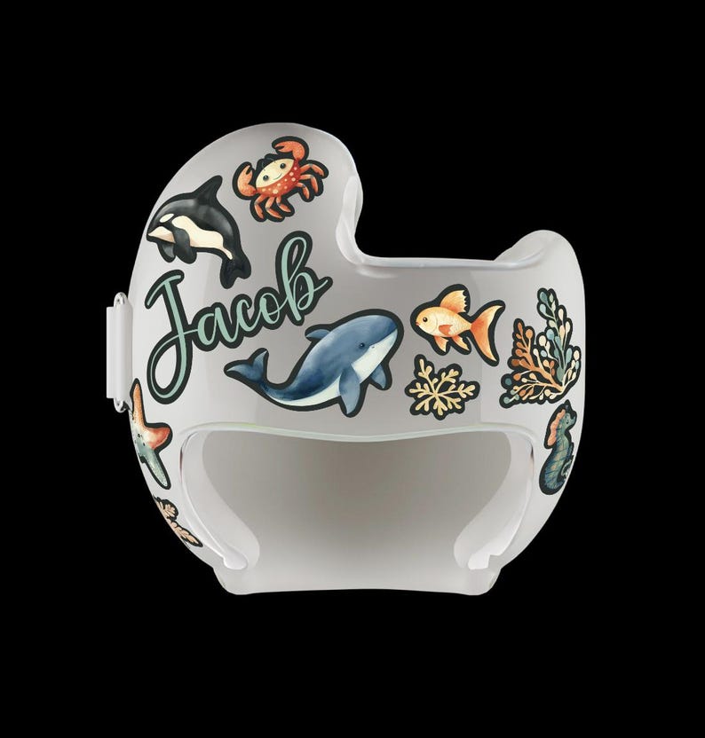 Op de afbeelding: Een witte helm met stickers van een blauwe walvis, een oranje vis, een krab en zeewier. De helm heeft de naam "Jacob" erop.