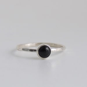 May include: A silver ring with a black gemstone. The ring has a hammered texture.