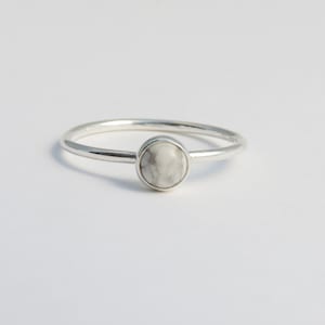 May include: A silver ring with a white howlite gemstone. The ring is simple and elegant.