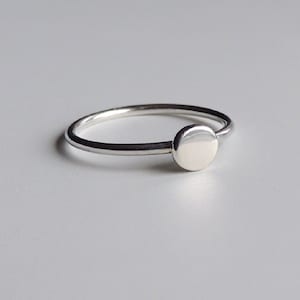 May include: A simple silver ring with a round, flat top.