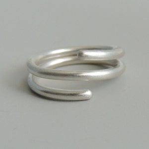 May include: A silver ring with a double band design. The ring is made of two bands that are twisted together.