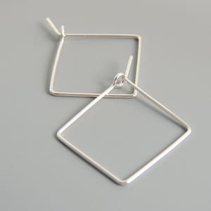 Può includere: Un paio di orecchini a cerchio quadrati in argento. Gli orecchini sono semplici ed eleganti e sarebbero un'ottima aggiunta a qualsiasi collezione di gioielli.