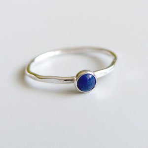 Puede incluir: Un anillo de plata con una piedra preciosa azul. El anillo tiene una textura martillada y un diseño simple.