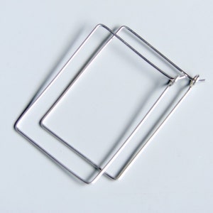 Könnte beinhalten: Ein Paar silberne quadratische Creolen. Die Ohrringe sind aus dünnem Metall gefertigt und haben ein schlichtes, modernes Design.