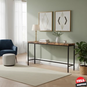 May include: A rectangular console table with a wood-grain surface and a black metal frame. The table is positioned against a wall featuring two framed geometric prints, a table lamp with a white shade, a white vase with greenery, and a candle.
