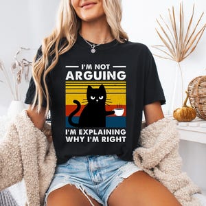 May include: Black t-shirt with a retro-style graphic of a black cat holding a cup of coffee. The text on the shirt reads "I'm not arguing, I'm explaining why I'm right."