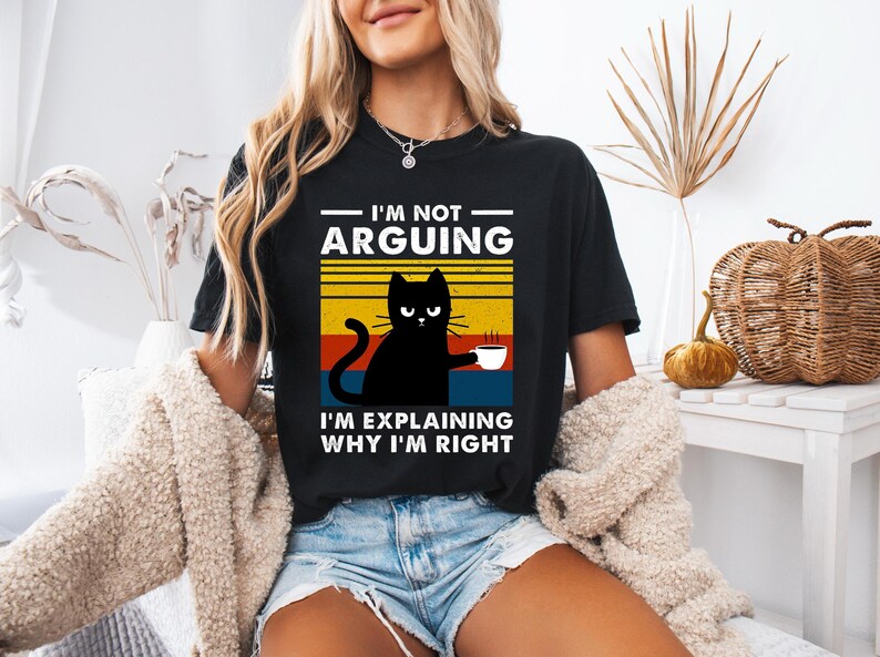 May include: Black t-shirt with a retro-style graphic of a black cat holding a cup of coffee. The text on the shirt reads "I'm not arguing, I'm explaining why I'm right."