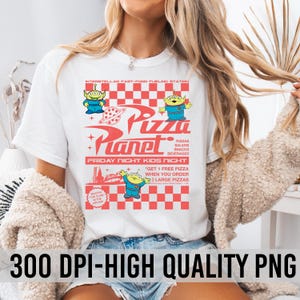May include: White t-shirt with a graphic print of a retro-style pizza restaurant called "Pizza Planet" featuring characters from the movie Toy Story. The text on the shirt reads "Interstellar Fast-Food Fueling Station", "Pizza Planet", "Friday Night Kids Night", "Pizzas, Salads, Snacks, Beverages", and "Get 1 Free Pizza When You Order 2 Large Pizzas".