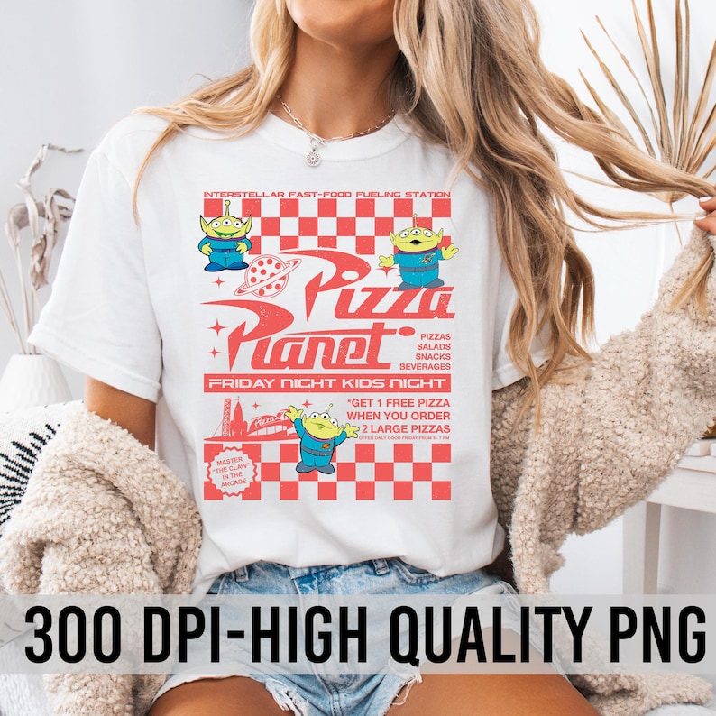 May include: White t-shirt with a graphic print of a retro-style pizza restaurant called "Pizza Planet" featuring characters from the movie Toy Story. The text on the shirt reads "Interstellar Fast-Food Fueling Station", "Pizza Planet", "Friday Night Kids Night", "Pizzas, Salads, Snacks, Beverages", and "Get 1 Free Pizza When You Order 2 Large Pizzas".