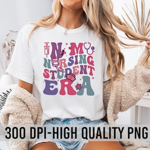 May include: A white t-shirt with a graphic design that says "In My Nursing Student Era". The graphic is in a retro style with colorful letters and medical symbols.