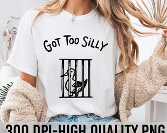 Op de afbeelding: Wit T-shirt met zwarte tekst die "Got Too Silly" zegt en een zwart-witte illustratie van een eend in een kooi.