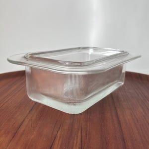 May include: A clear glass rectangular dish with a lid. The dish has a ribbed texture and a slightly rounded edge.