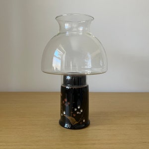 May include: A clear glass lampshade with a black base decorated with gold and white floral designs. The lampshade is shaped like a mushroom.