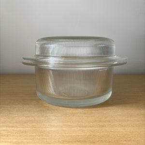 May include: A clear glass storage container with a lid. The container has a ribbed design and is perfect for storing food.
