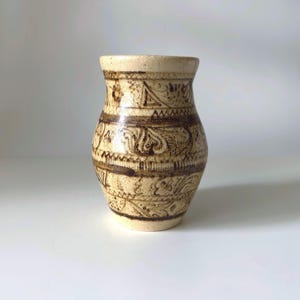 May include: A small, cream-colored ceramic vase with a brown geometric and floral design.