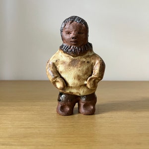 May include: A ceramic figurine of a person wearing a brown sweater and brown pants. The figurine has a brown face and a brown beard.