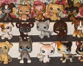 May include: A collection of twenty small plastic animal figurines arranged on a three-tiered display stand. The figures include various dogs, cats, and other creatures with large eyes, painted in diverse colors such as brown, white, gray, and tan.