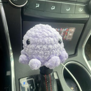 May include: A purple crocheted octopus gear shift knob for a car.