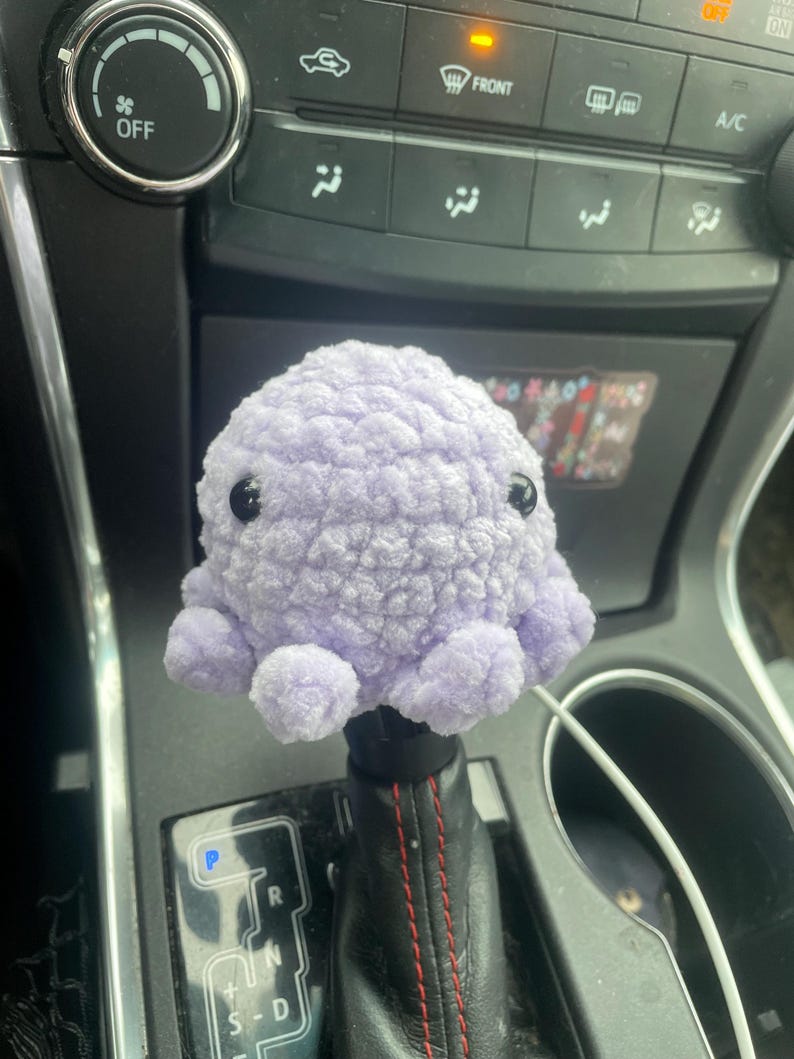 May include: A purple crocheted octopus gear shift knob for a car.