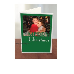 May include: A green Christmas card with a photo of two boys in front of a Christmas tree. The card says "Merry Christmas" in white letters.