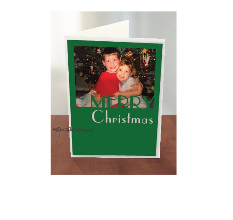 May include: A green Christmas card with a photo of two boys in front of a Christmas tree. The card says "Merry Christmas" in white letters.