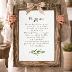 May include: A rectangular wooden frame with a textured brown finish, featuring a beige fabric bow at the top and a white print of Philippians 4:6-7. The text is black, and a small watercolor illustration of an olive branch is at the bottom.