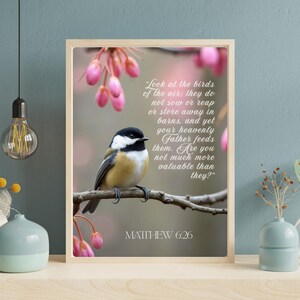 Op de afbeelding: Een ingelijste print met een kleine vogel op een tak, met roze bloesems op de achtergrond. De tekst luidt: "Look at the birds of the air... Mattheüs 6:26". De vogel heeft zwarte, witte en gele veren.